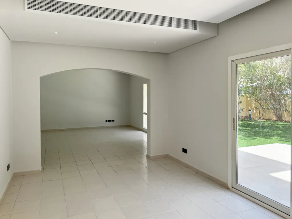 Empty room with white walls, tile floor, and arched doorway. Sliding glass door leads to a green lawn.