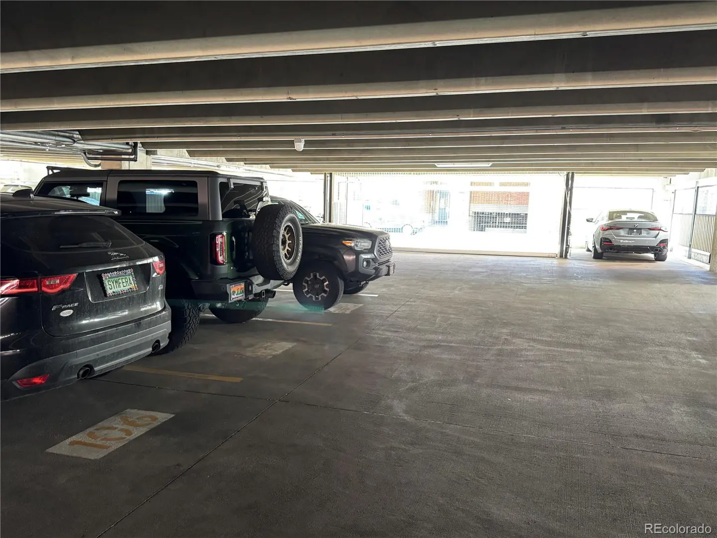 Indoor parking garage with parked cars. A black SUV is parked on the left, a black truck in the middle, and a gray car in the distance.