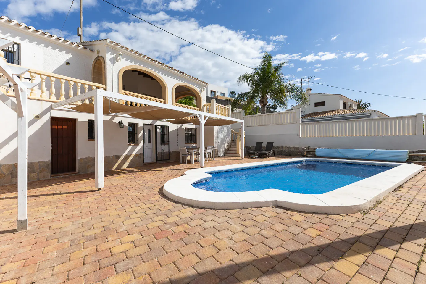 Exterior of a white two-story house with a blue swimming pool and brick patio under a sunny sky.
