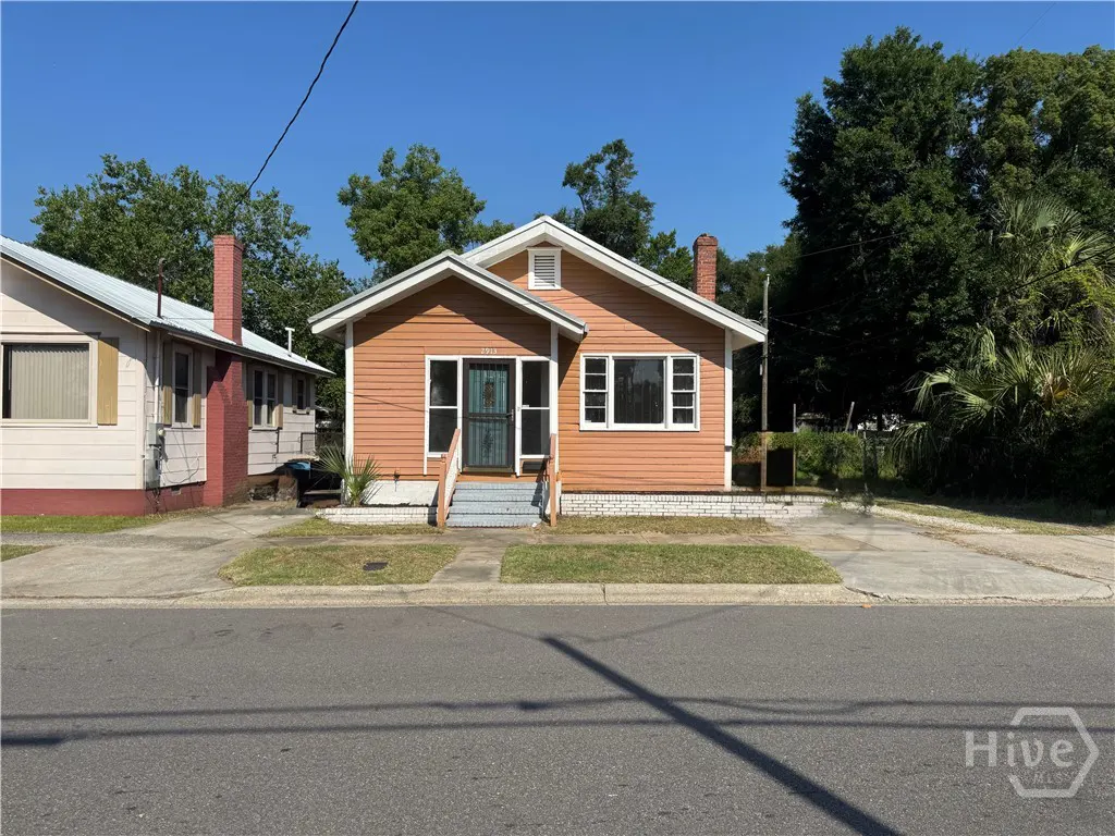 A single-story peach-colored house with a white trim, front porch steps, and a concrete driveway under a clear blue sky.