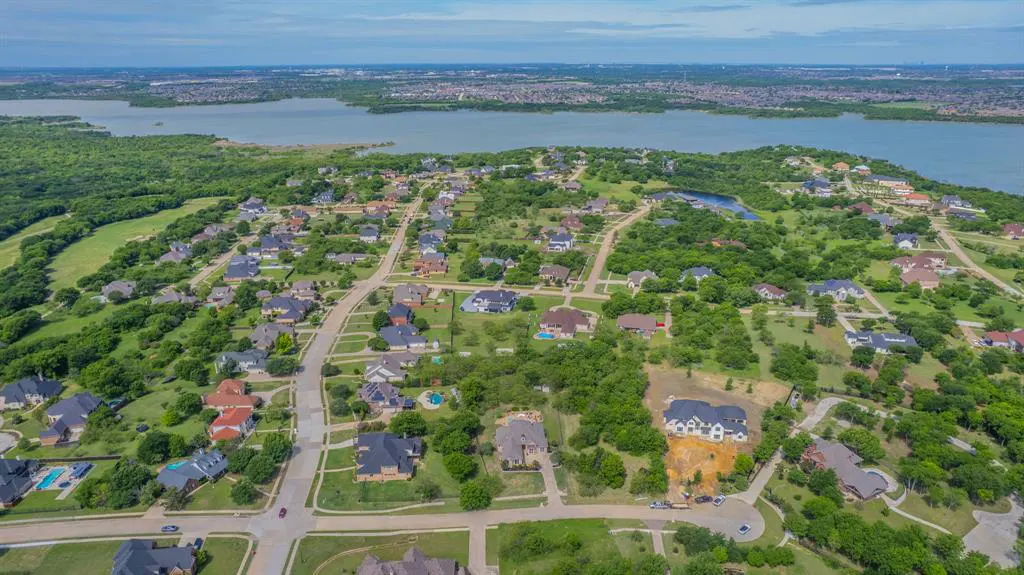 Aerial view of a residential area with houses, green trees, and a lake in the background.