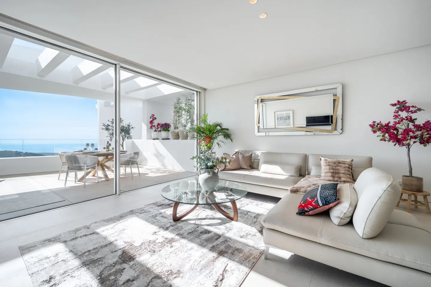 Bright living room with a beige sofa, glass table, and a patio with ocean views through large sliding glass doors.