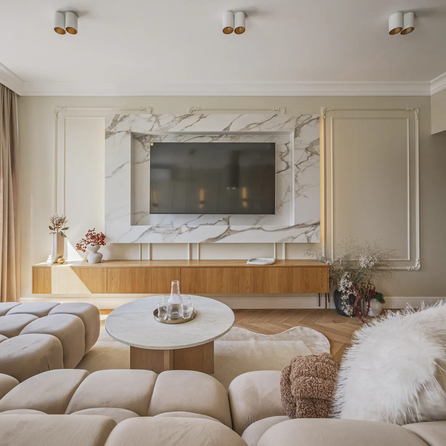 Living room with a beige sectional sofa, round marble coffee table, and a TV mounted on a marble wall.