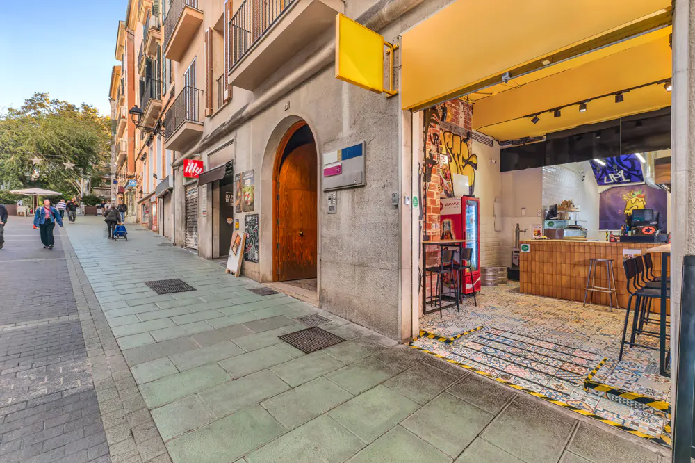 Street view of a restaurant with a yellow awning and open front. The interior has a counter, stools, and graffiti art.
