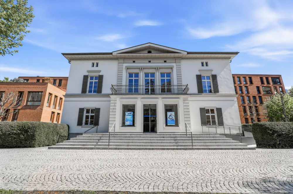 Exterior view of a white, two-story building with dark shutters and a gray stone staircase leading to the entrance.