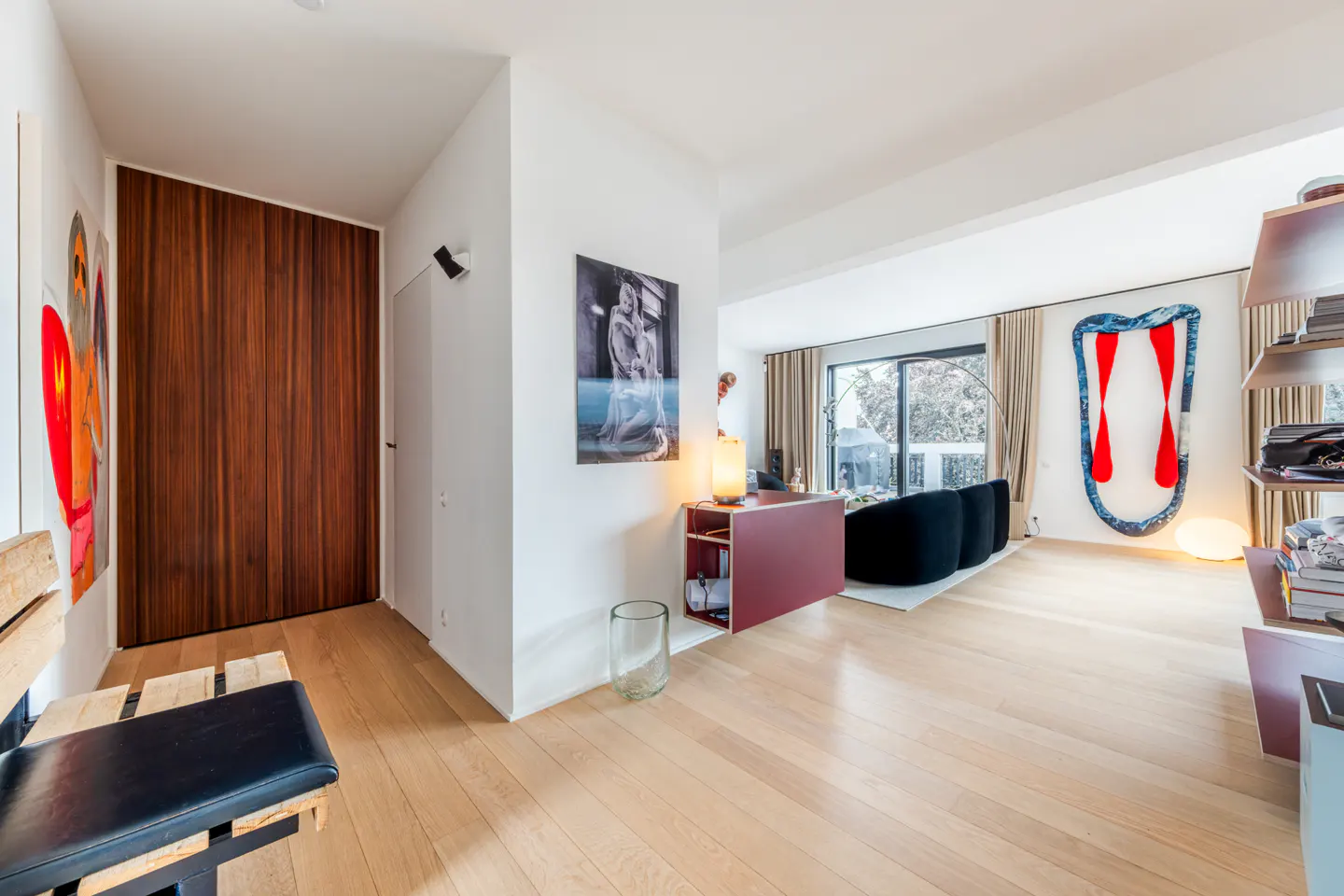 Modern living room with light wood floors, a maroon floating console, black curved sofa, and abstract wall art.