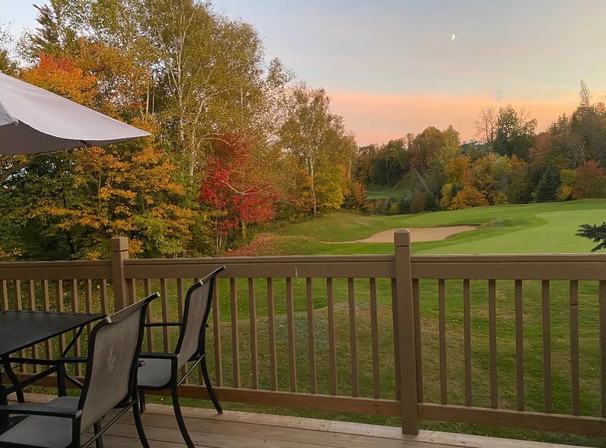 View from a wooden deck with table and chairs overlooking a golf course in autumn at sunset.