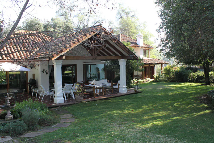 Exterior view of a two-story house with a red tile roof, a covered patio with white columns, and a green lawn.