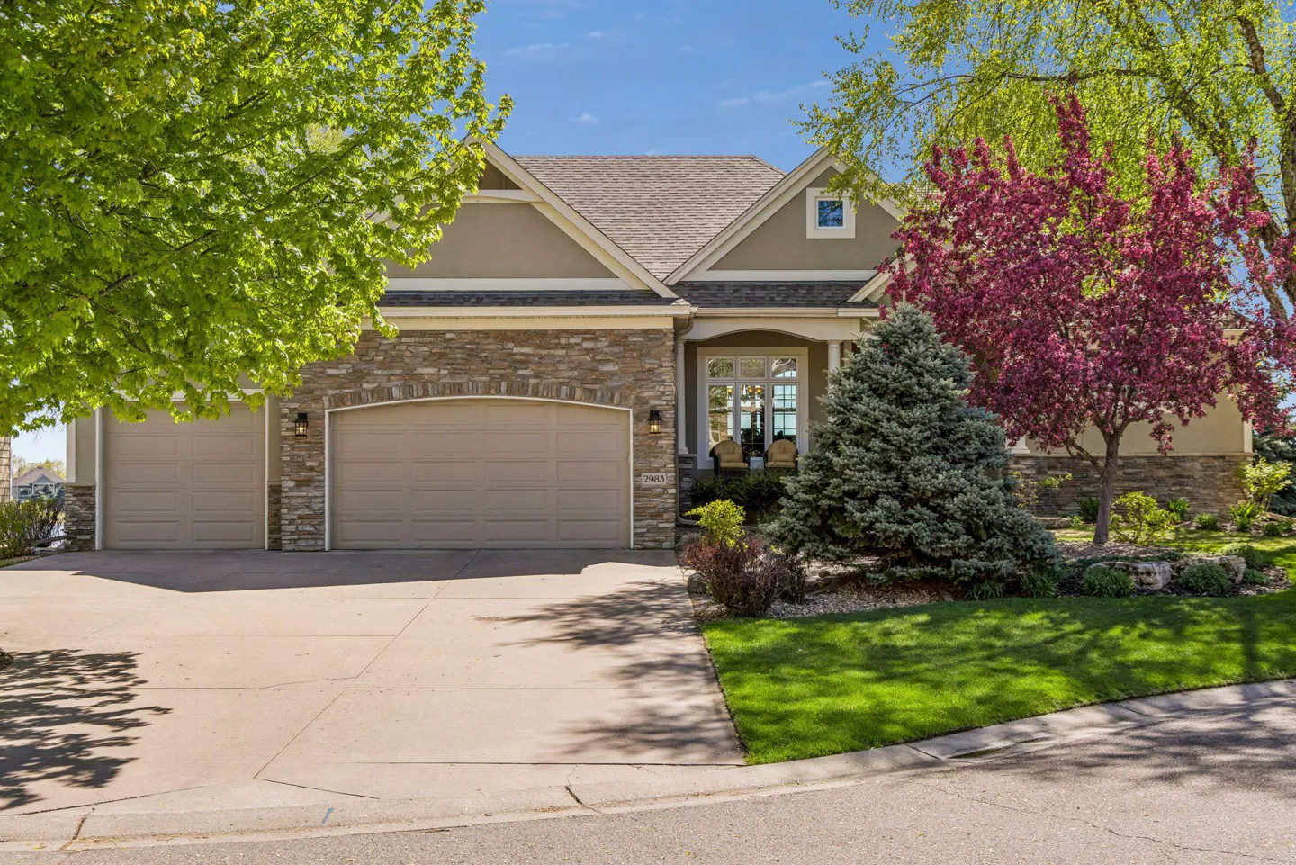Tan two-story house with a stone and stucco facade, a three-car garage, and manicured landscaping.