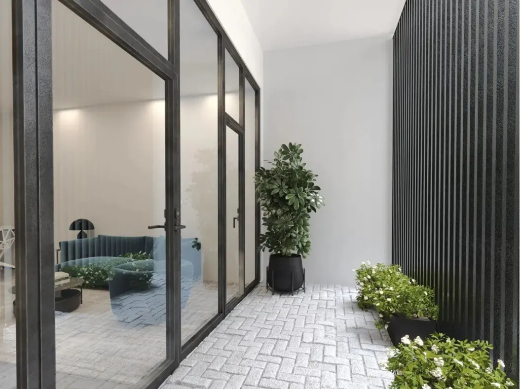 Modern patio with light stone pavers, potted plants, and black slatted walls, looking into a living room through glass doors.