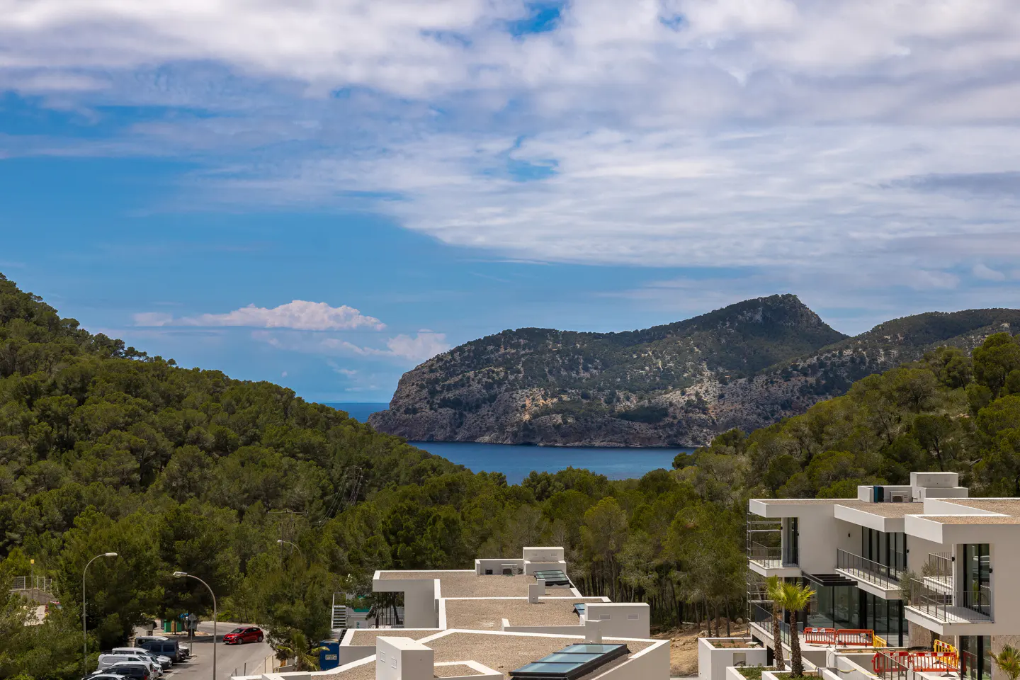 Scenic view of modern white buildings overlooking a lush green forest, blue ocean, and cloudy sky.