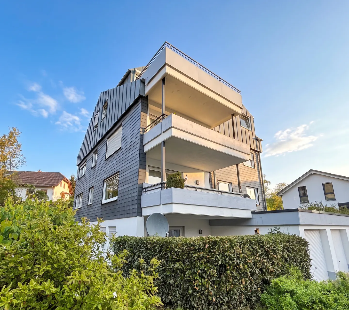Exterior view of a modern, multi-story apartment building with gray siding and white balconies against a blue sky.