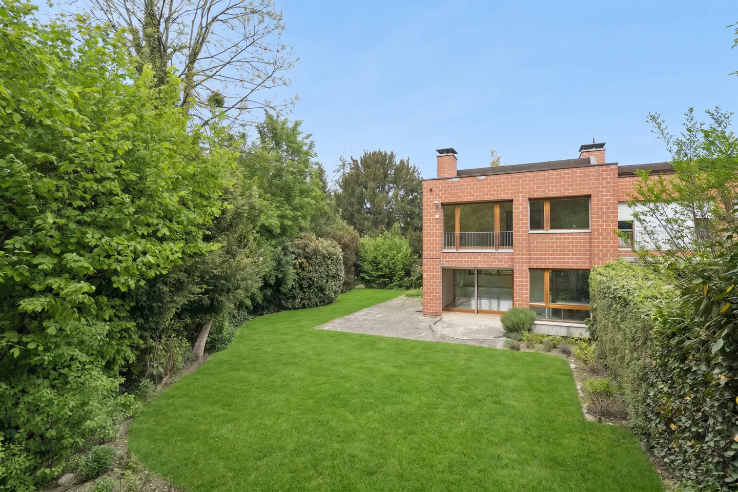 Two-story brick house with a green lawn and trees under a blue sky.