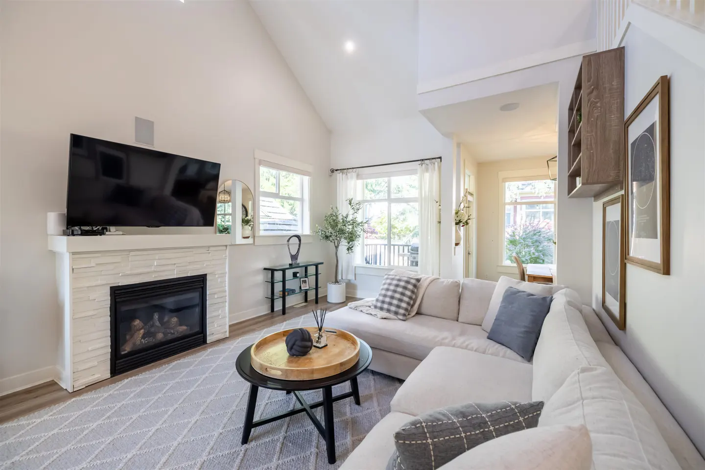 Bright living room with white walls, a fireplace with a TV above, and a large white sectional sofa. A black coffee table sits on a gray patterned rug.