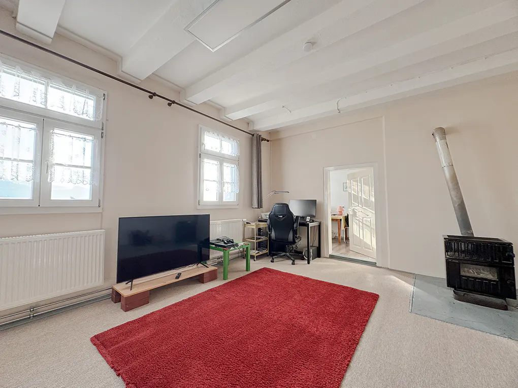 A living room with white walls, a red rug, a black TV, a desk, and a wood-burning stove.