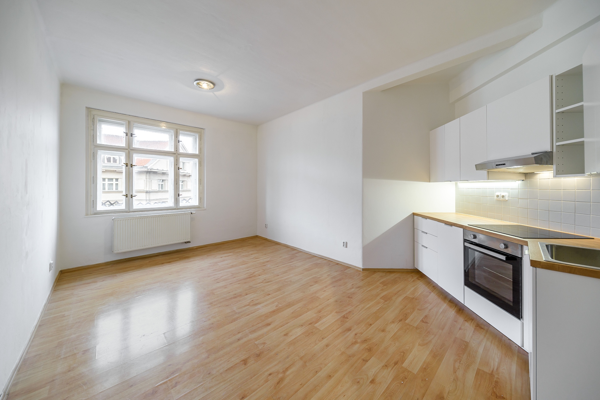 Bright studio apartment with white cabinets, light wood floors, and a large window overlooking a city street. [AI-generated text]