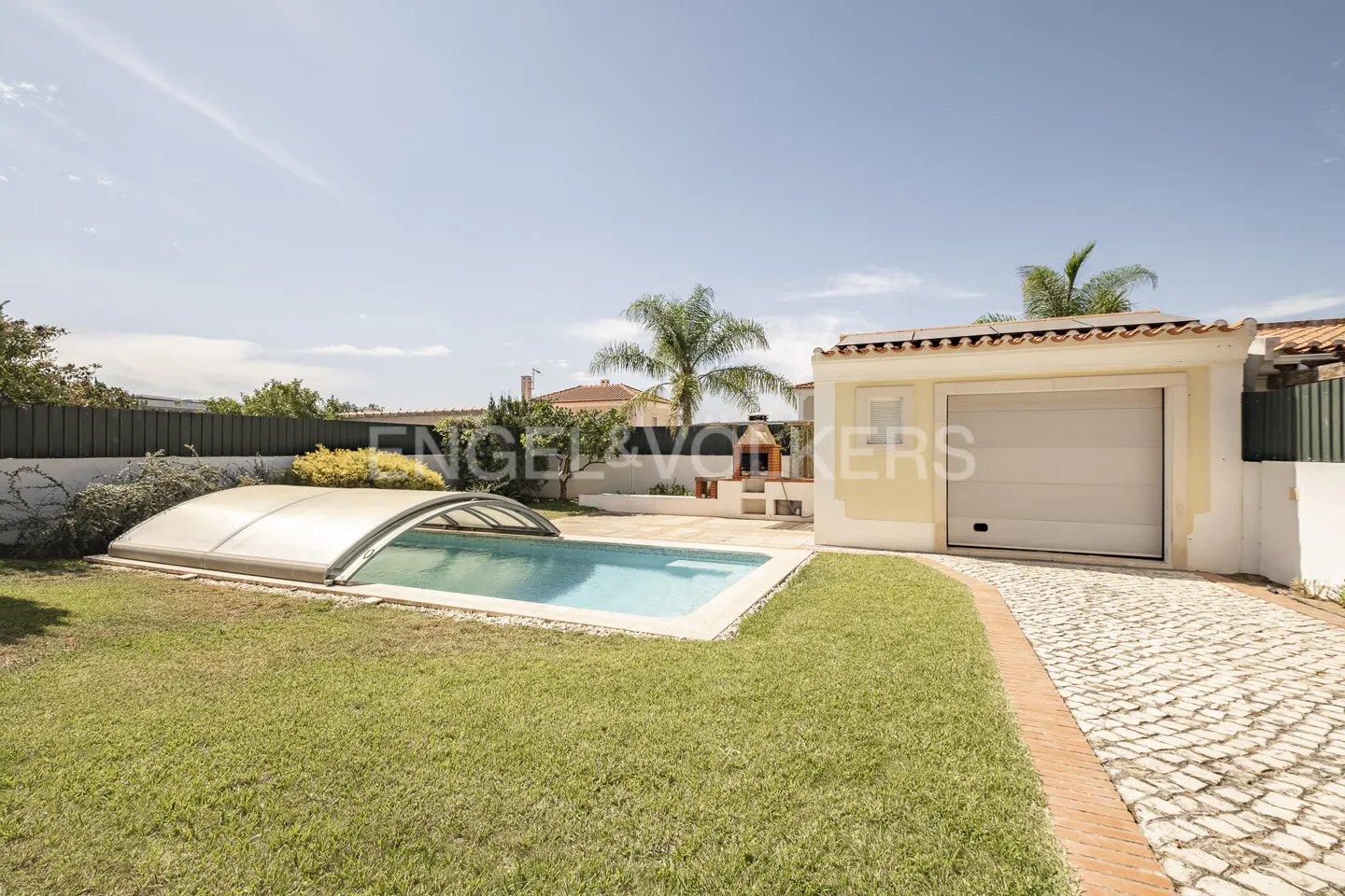 Backyard with a swimming pool under a retractable cover, a grassy lawn, a stone driveway, and a small outdoor grill area.