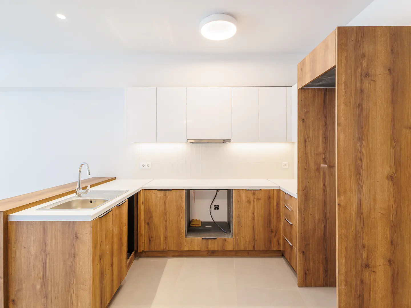 Modern kitchen with wood-grain lower cabinets, white upper cabinets, white countertops, and a stainless steel sink.