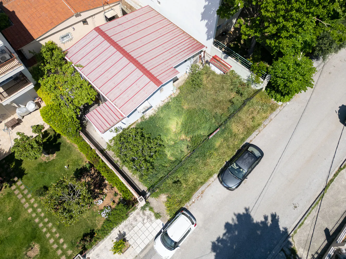 Aerial view of a house with a red roof, green lawn, and two cars parked on the street.