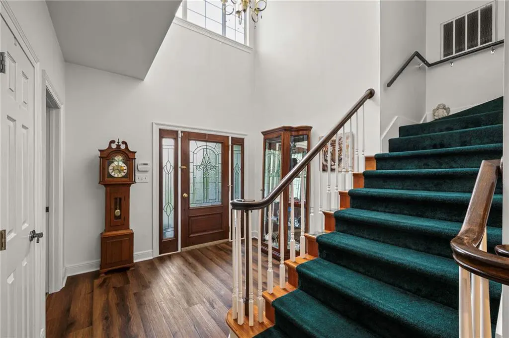 Foyer with a dark wood front door, grandfather clock, and green carpeted stairs.
