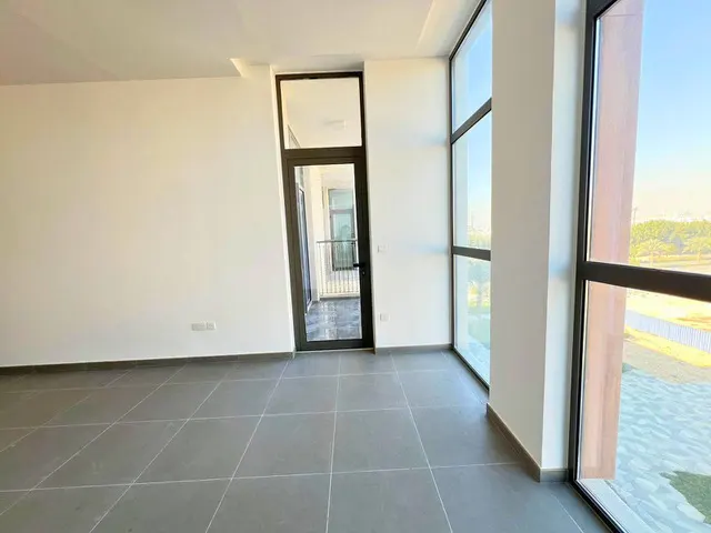 Empty room with gray tile floor, white walls, and black-framed windows and door to a balcony with a view.