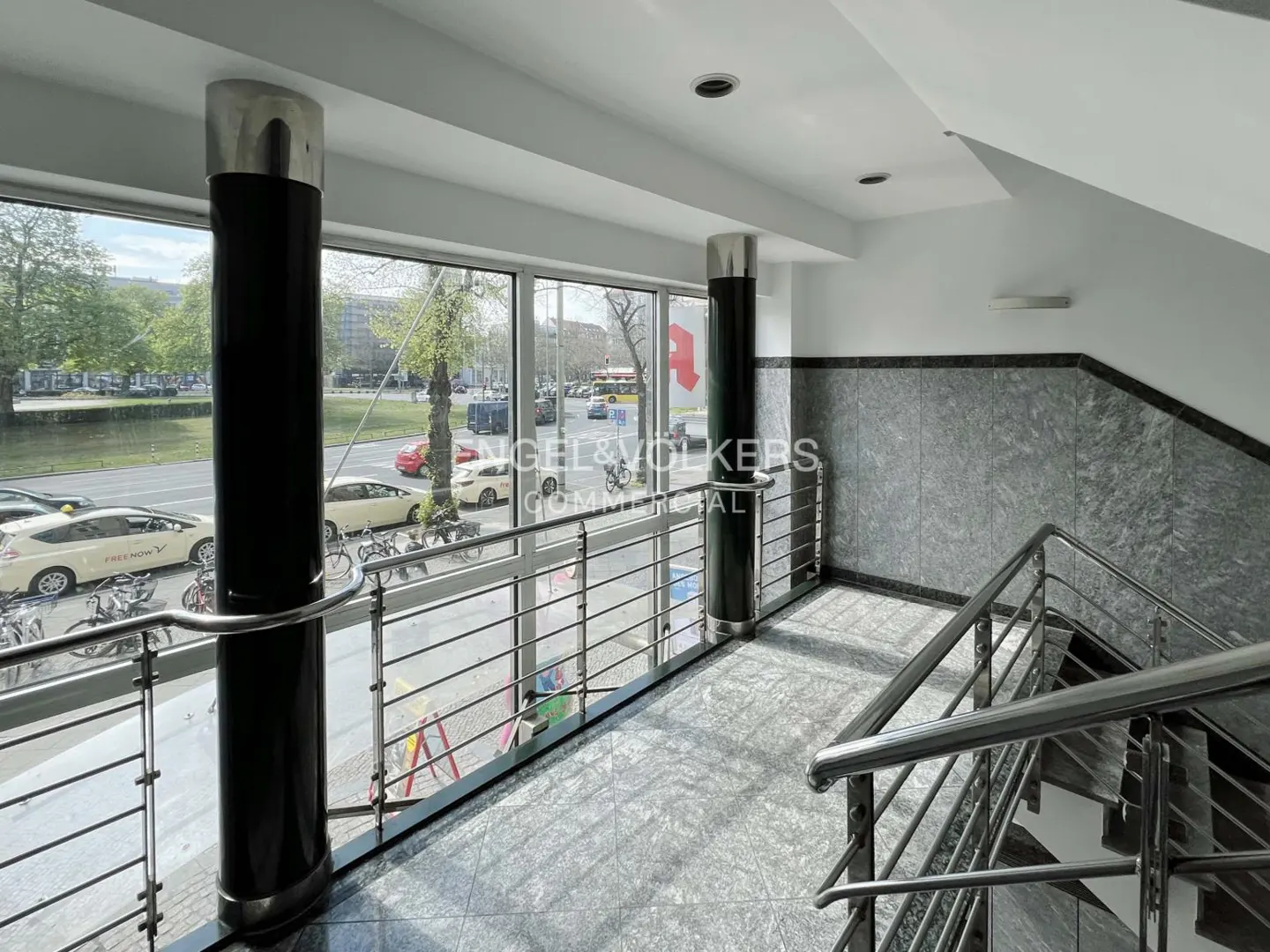 Interior view of a building with a staircase and a large window overlooking a street with cars and trees.