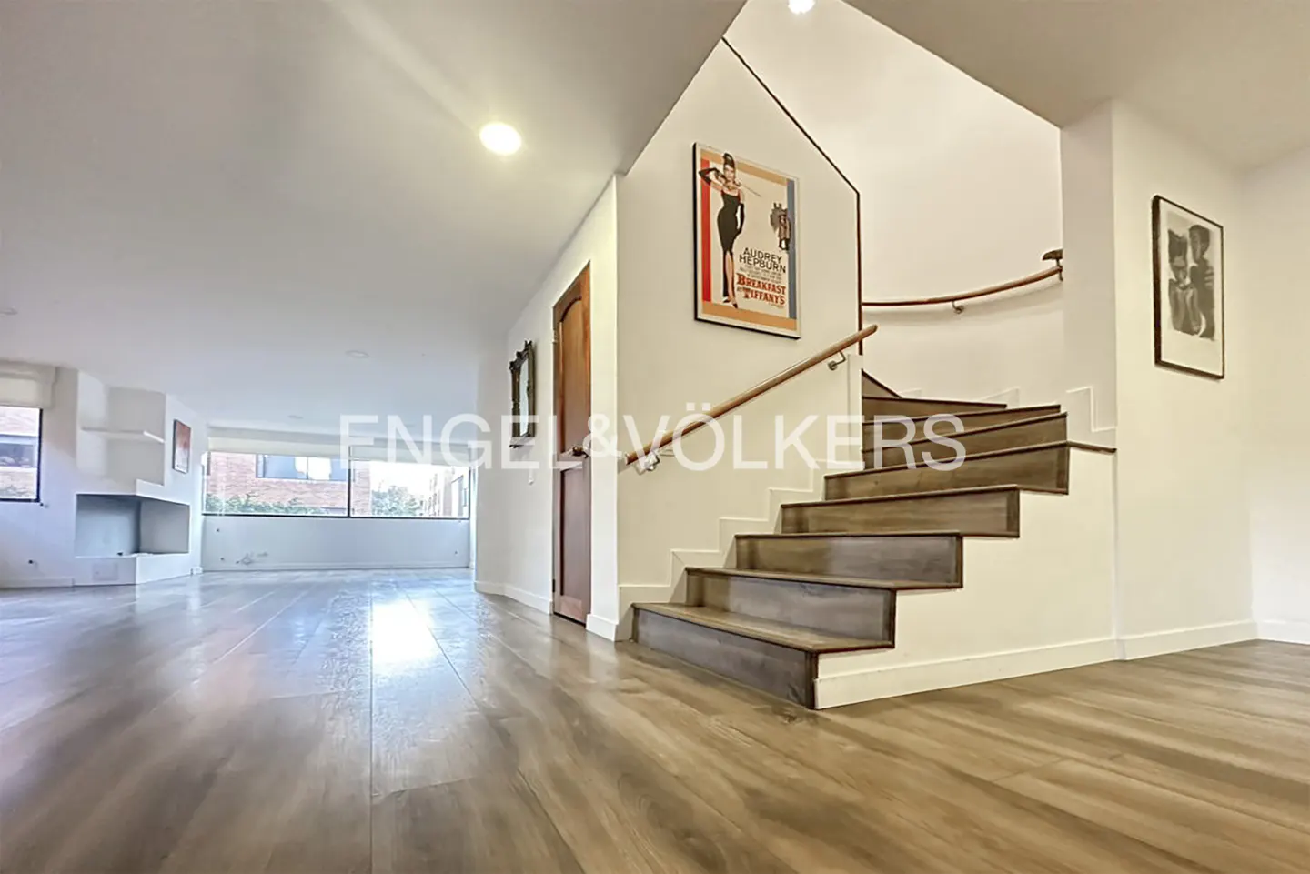 Bright, modern home interior with wood floors, white walls, and a staircase with a wooden handrail. Artwork adorns the walls.