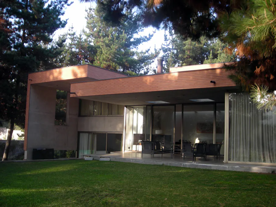 Modern house with a flat roof, large glass windows, and a green lawn. Trees surround the property.