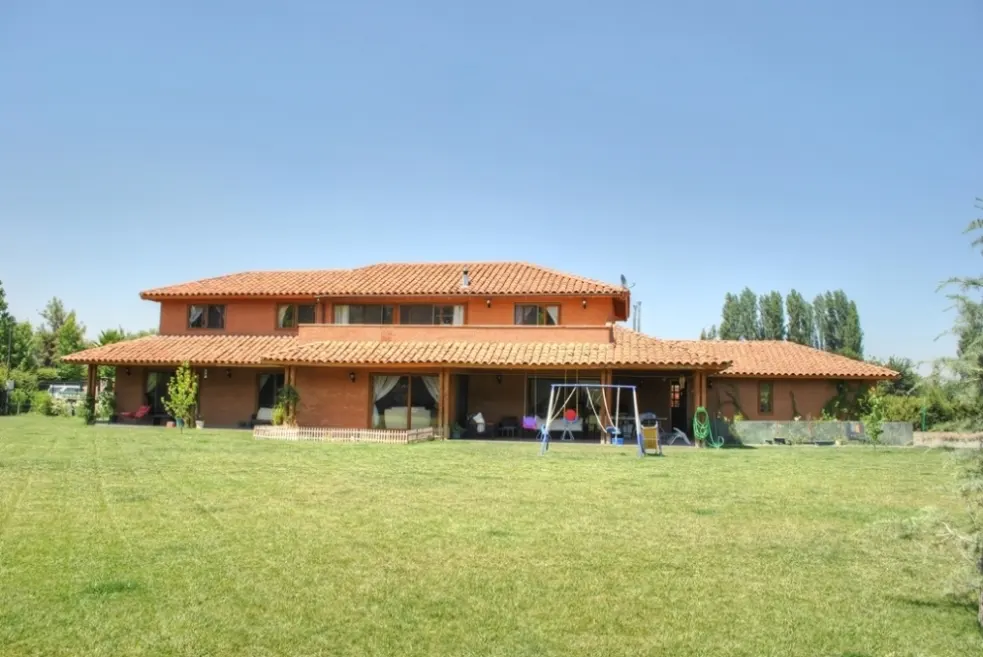 Two-story house with a red tile roof and a large green lawn under a clear blue sky. A swing set sits on the patio.