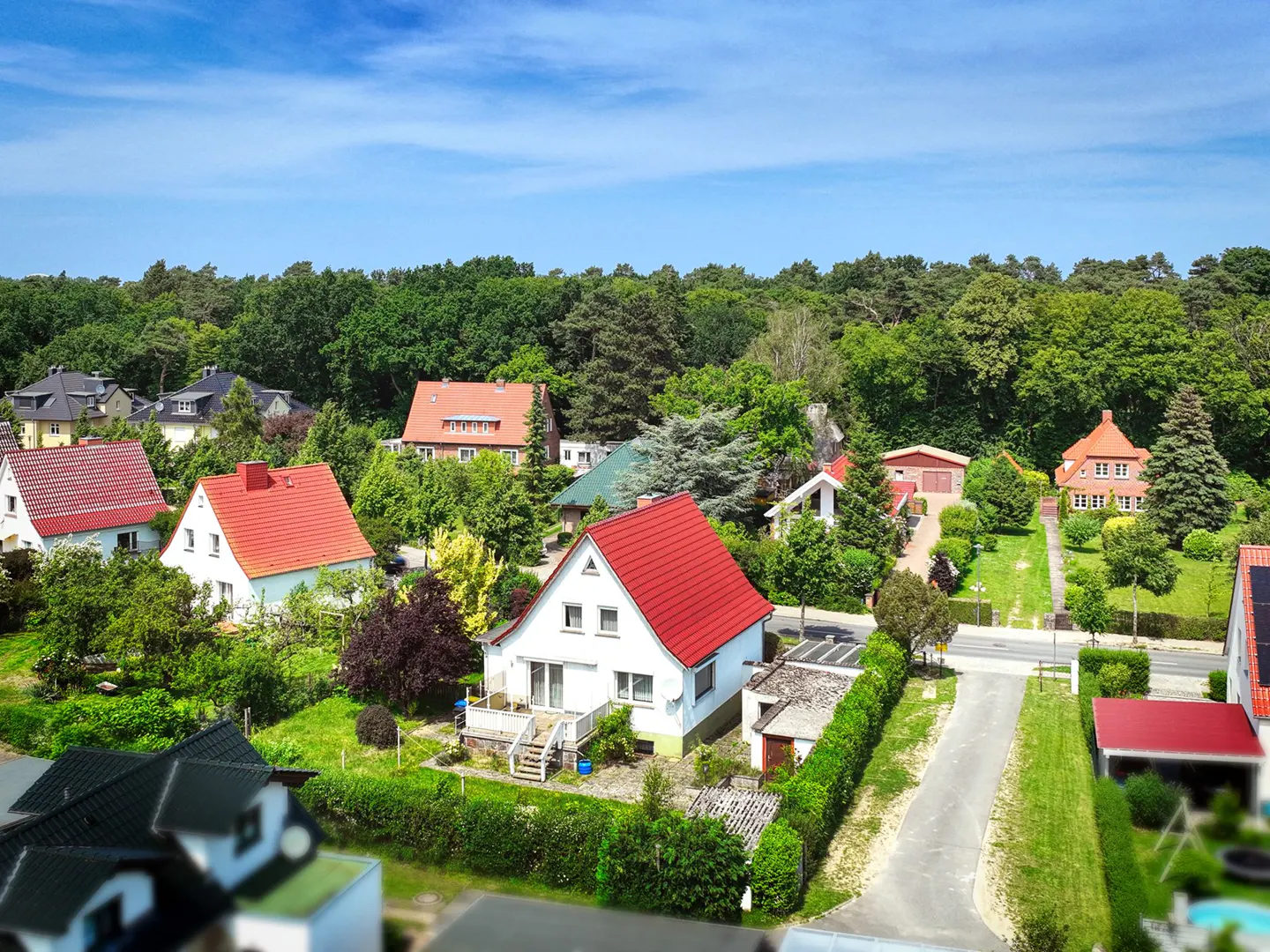 Aerial view of a neighborhood with houses with red roofs surrounded by green trees under a blue sky.