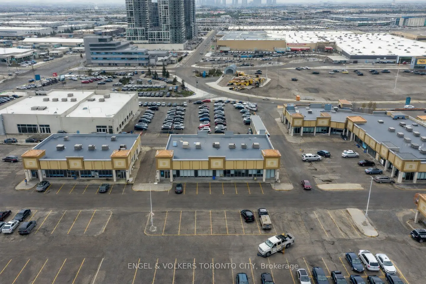 Aerial view of two tan commercial buildings with flat roofs surrounded by large parking lots in an urban area.