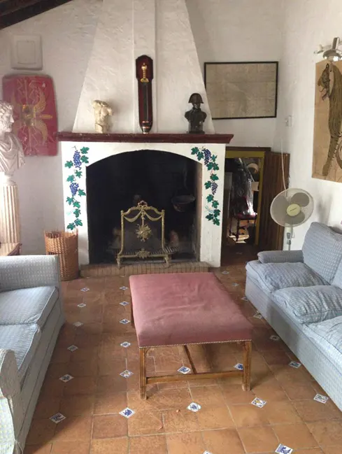 Living room with a large white fireplace decorated with grape vines, sofas, and a red ottoman on a tiled floor.