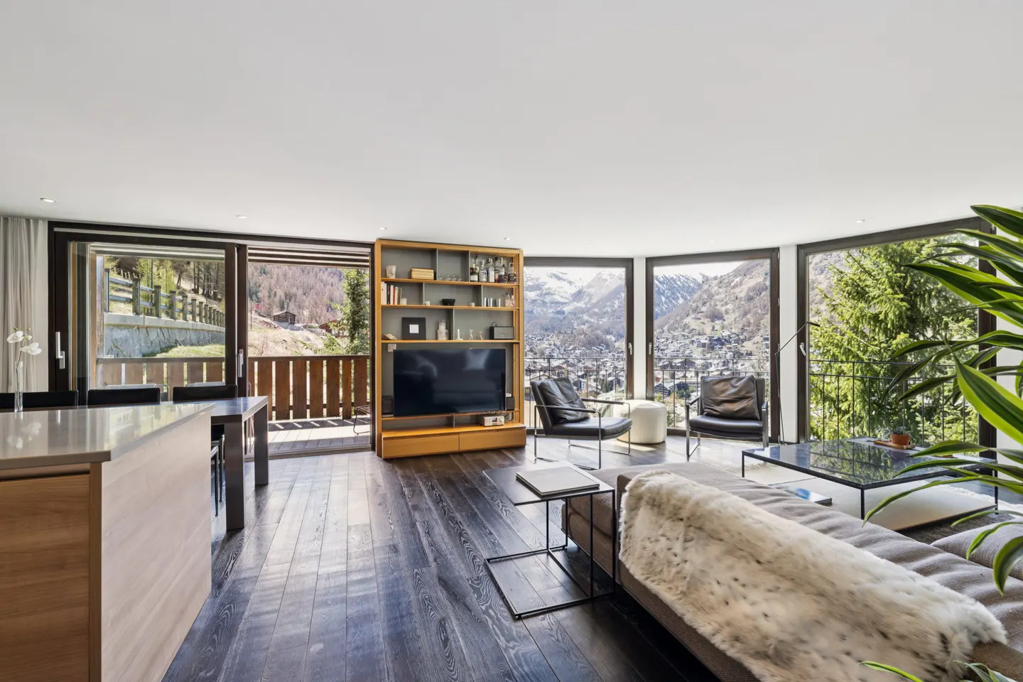 Bright living room with dark wood floors, a brown sofa with a white throw, and a view of snow-capped mountains.