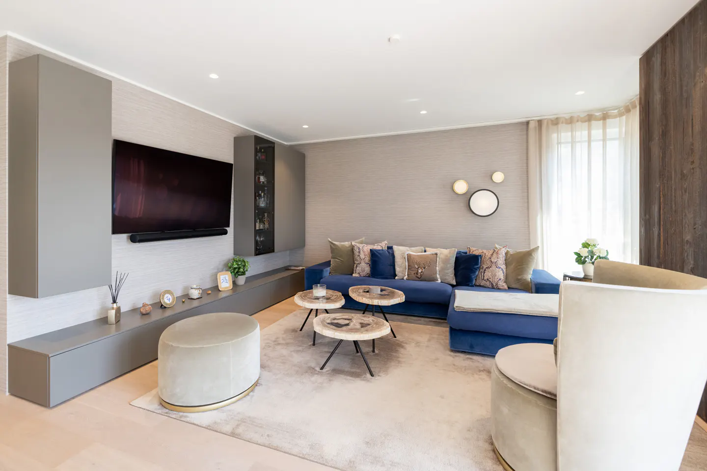 Living room with blue sectional sofa, wood-slice coffee tables, and gray built-in shelving with a TV.
