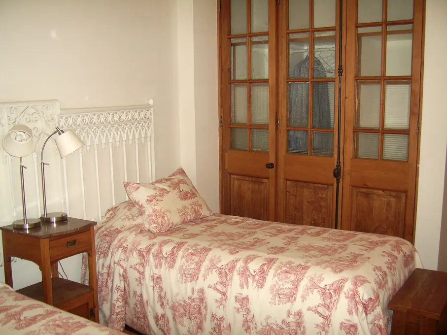 Bedroom with twin beds, white iron headboards, red toile bedding, wood nightstands with lamps, and wood closet doors with glass panes.