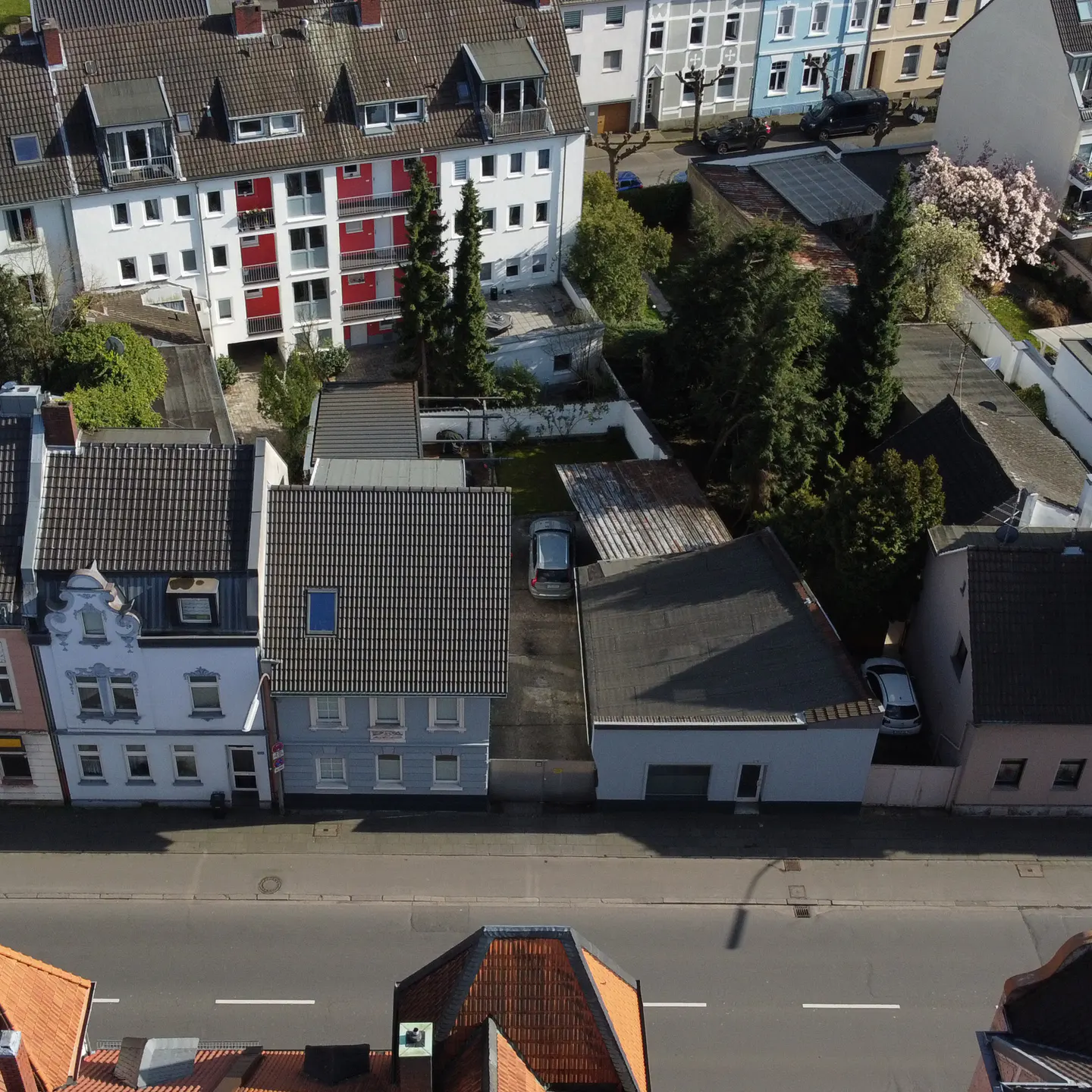 Aerial view of a street with houses, some with red accents, and trees in the backyards.