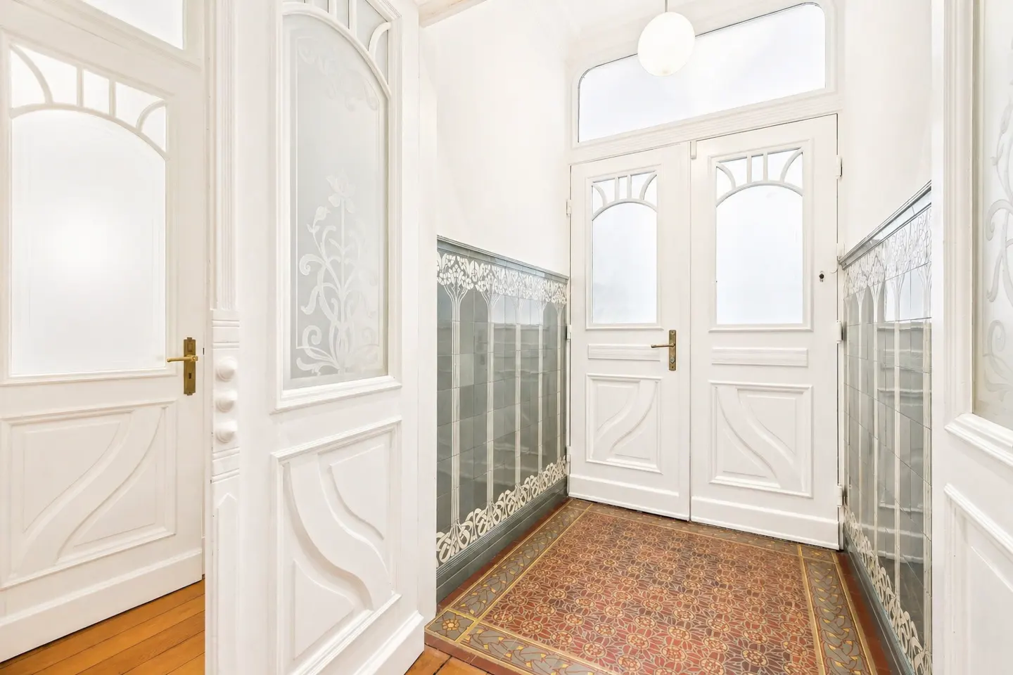 Bright hallway with white paneled doors, decorative frosted glass, and patterned tile floor and wall trim.