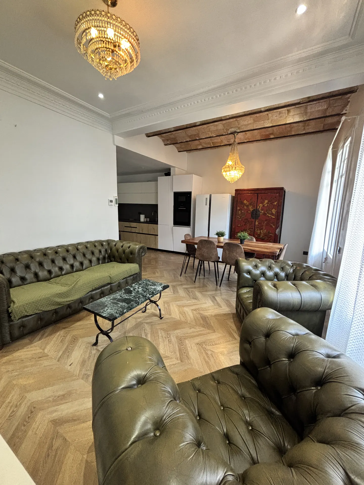 A wide shot of a living room with olive green leather sofas, a marble coffee table, and a dining area with a wooden table and chairs.