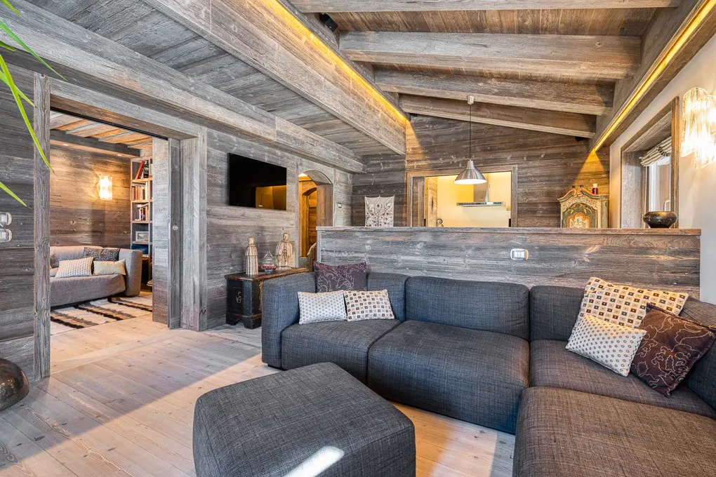 Living room with gray sectional sofa, wood paneled walls and ceiling, and light wood floors. A TV is mounted on the wall.