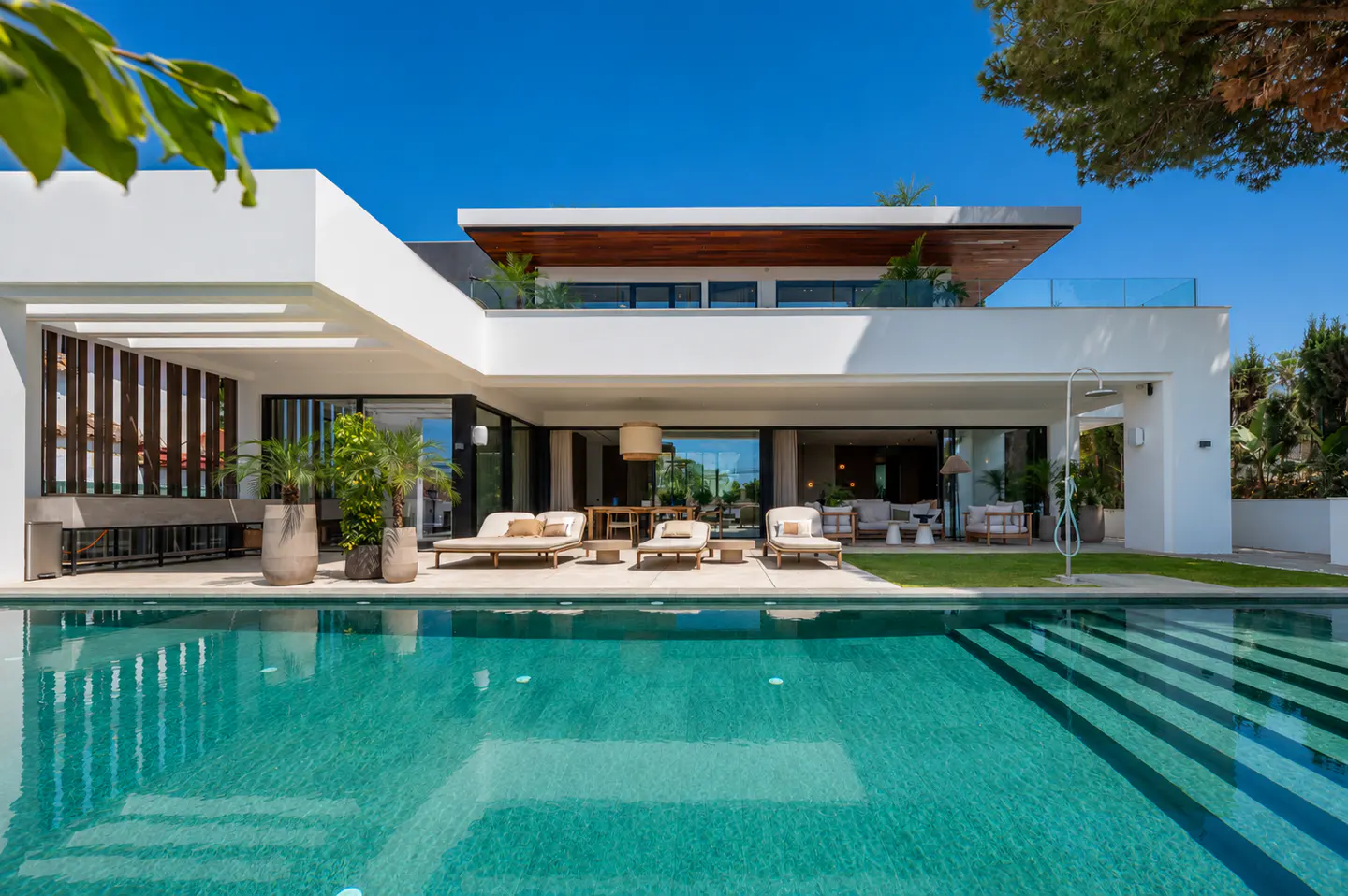 Modern white house with a turquoise pool in the foreground under a clear blue sky.