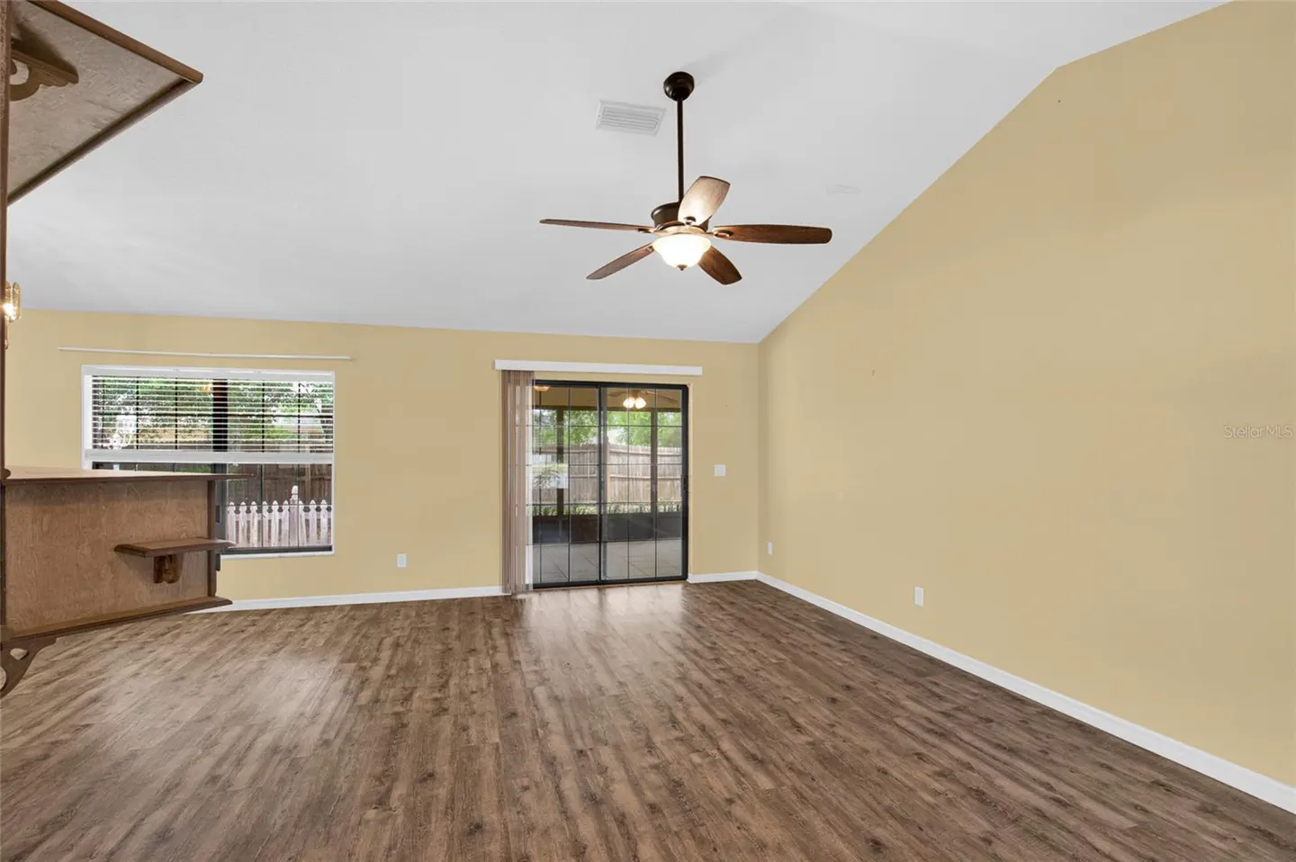 A living room with wood floors, yellow walls, a ceiling fan, and sliding glass doors.