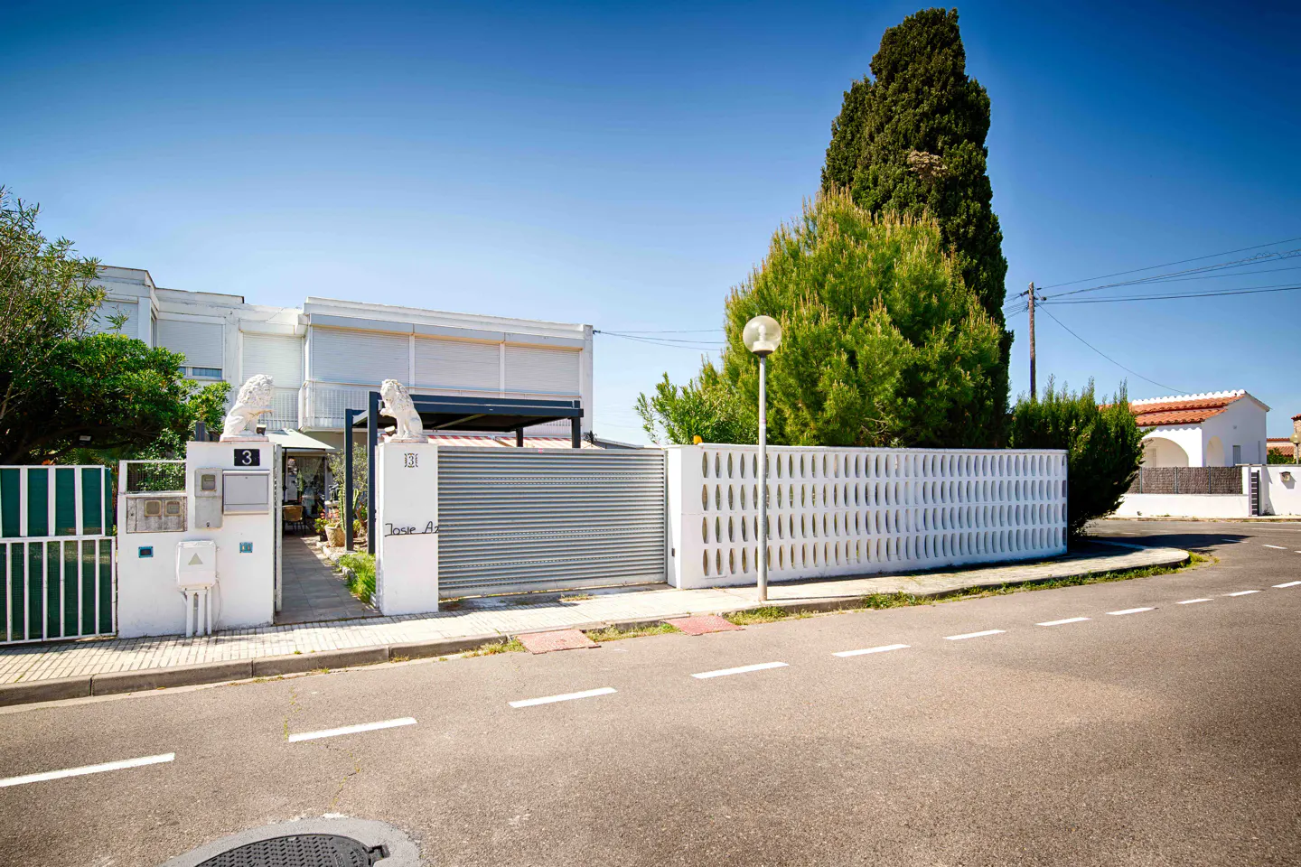 Exterior view of a white two-story house with a metal gate and white fence, street in front.
