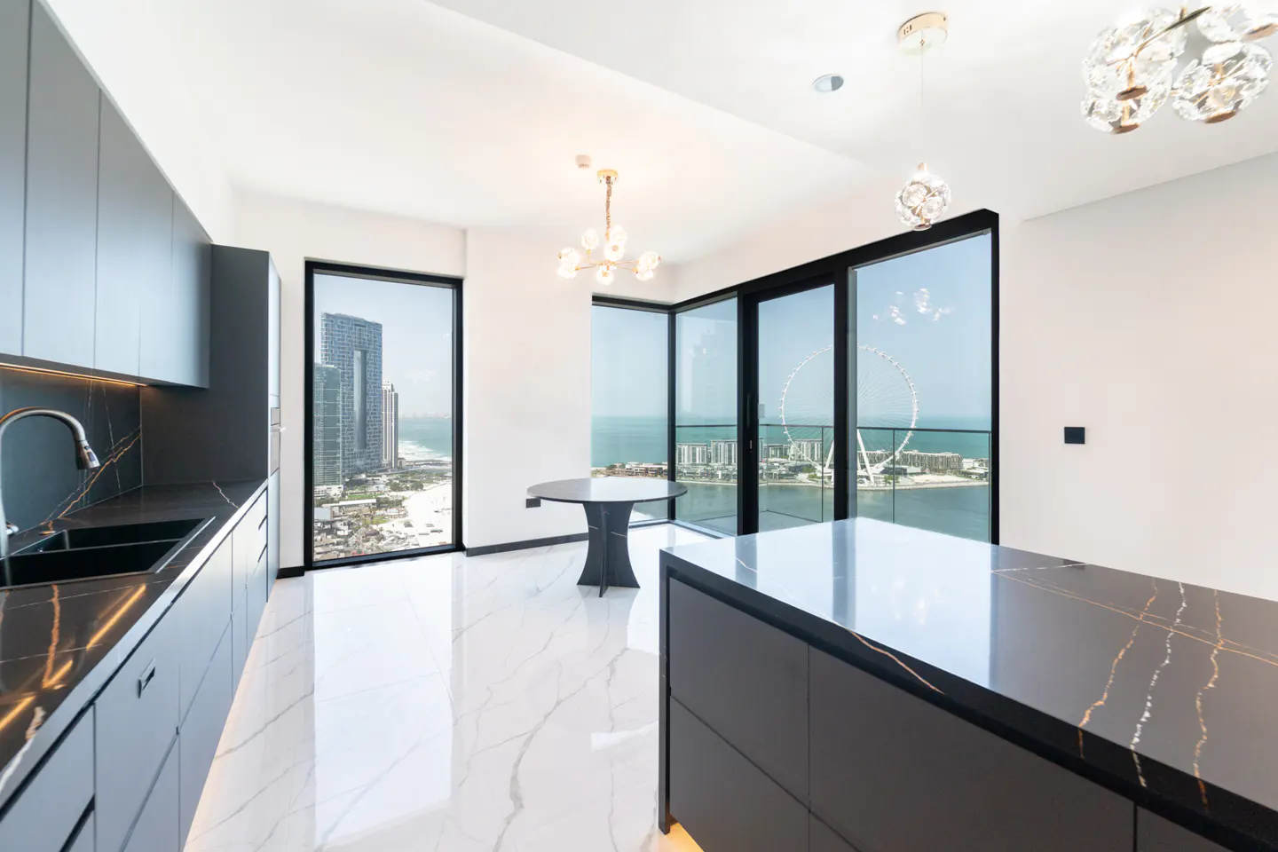 Modern kitchen with black cabinets, marble floors, and floor-to-ceiling windows overlooking a city skyline and ocean view.