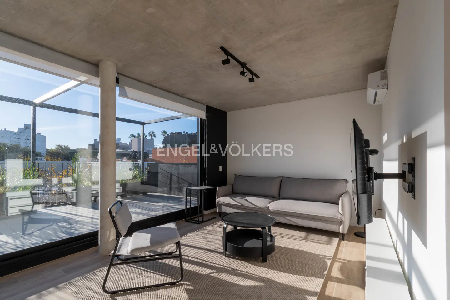 Bright living room with a gray sofa, black coffee table, and large windows leading to a balcony with city views.
