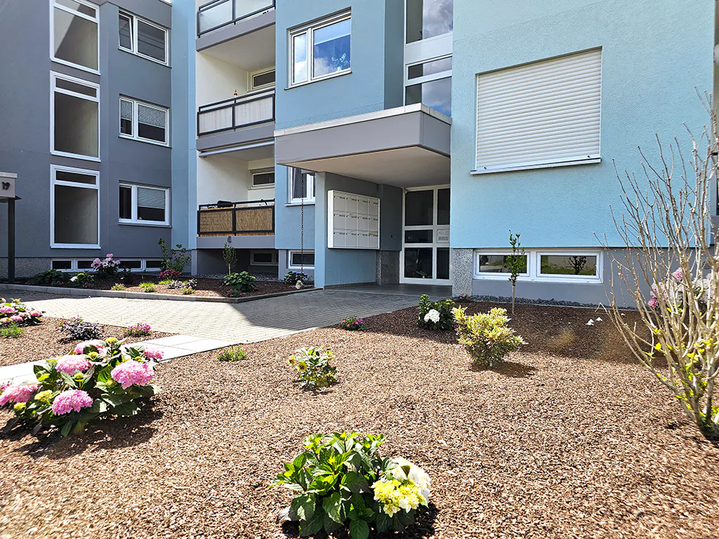 Exterior of a blue and gray apartment building with a garden and a paved walkway.