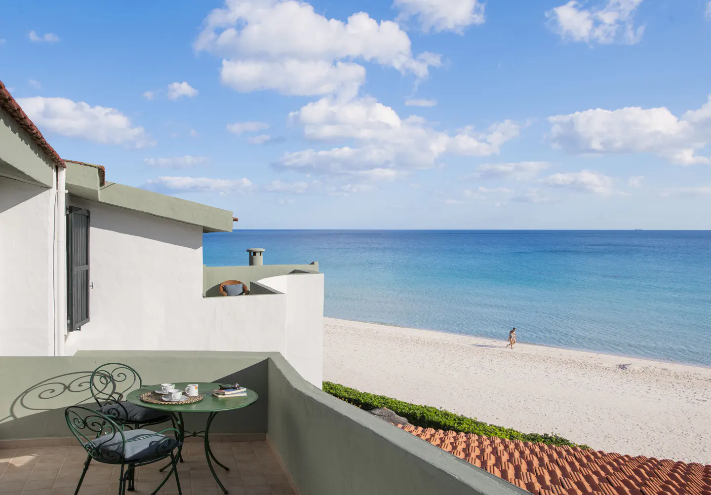 Balcony view of a white sand beach and turquoise ocean under a blue sky. A green table and chairs sit on the balcony.