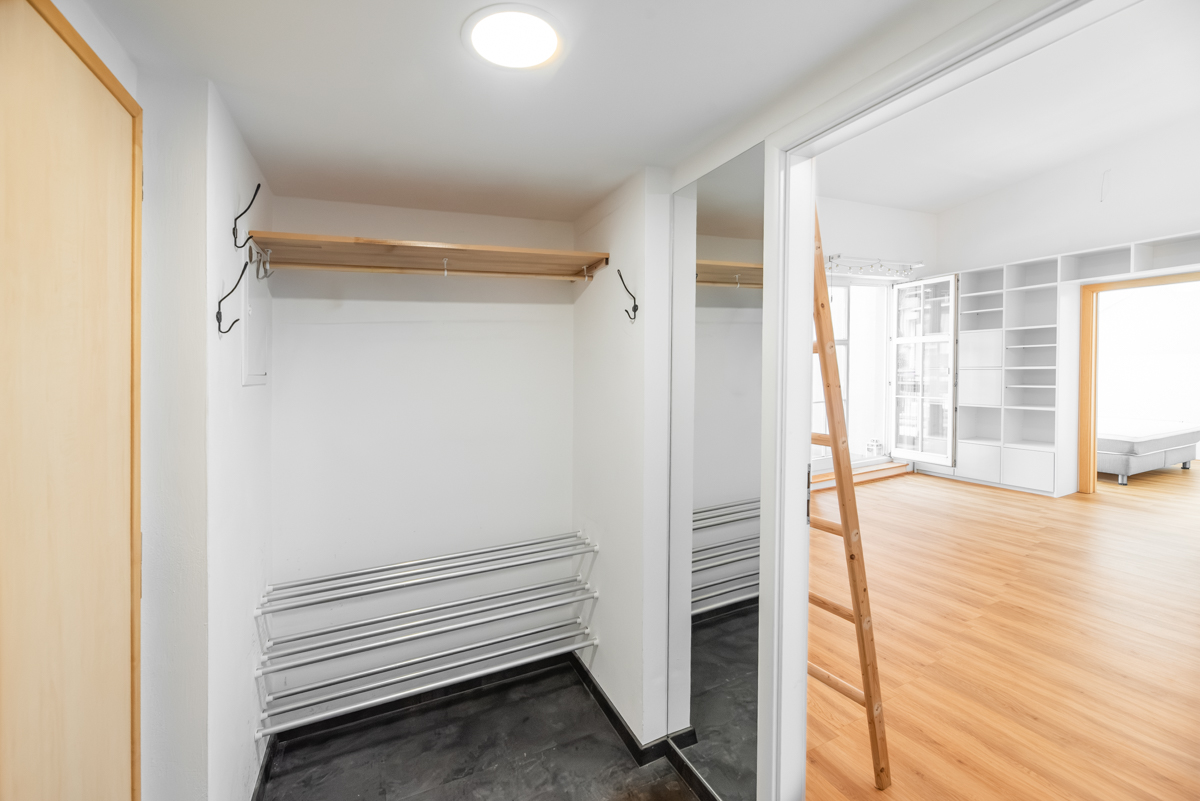 Entryway with a wooden shelf, metal shoe rack, and mirror, leading into a bright living room with light wood flooring.