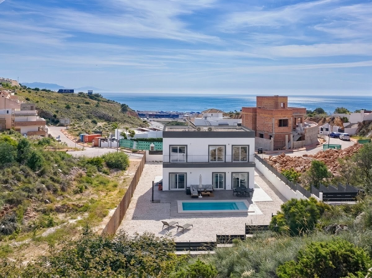 Modern two-story white villa with a swimming pool, patio furniture, and sea views in a coastal hillside neighborhood.