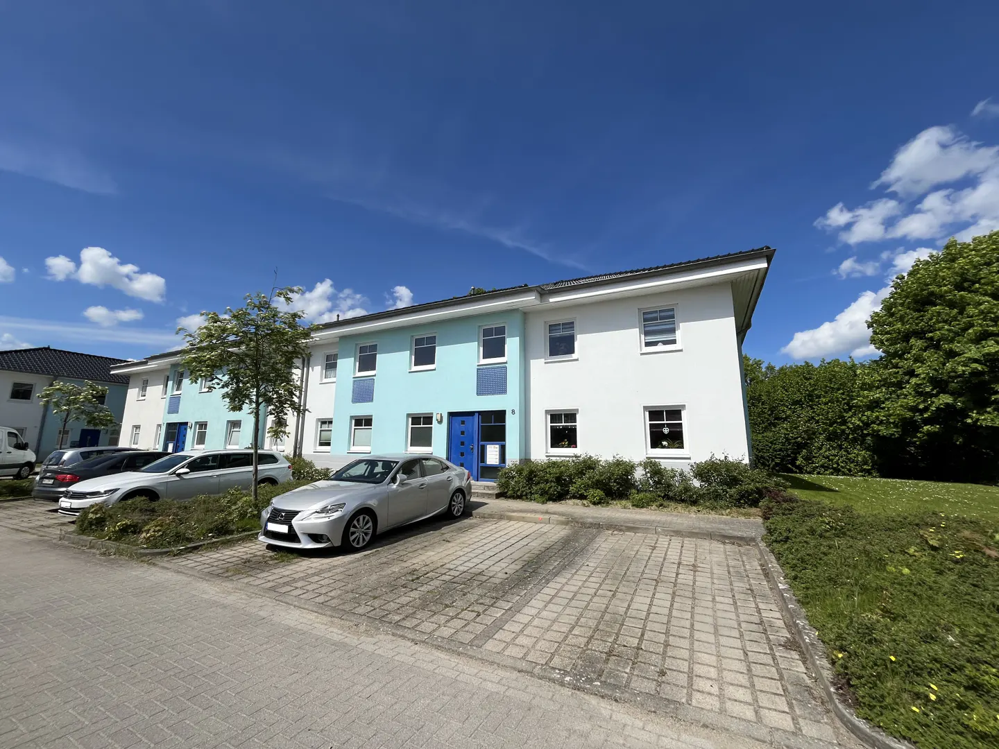 A two-story white and light blue apartment building under a clear blue sky with cars parked in the paved front lot.