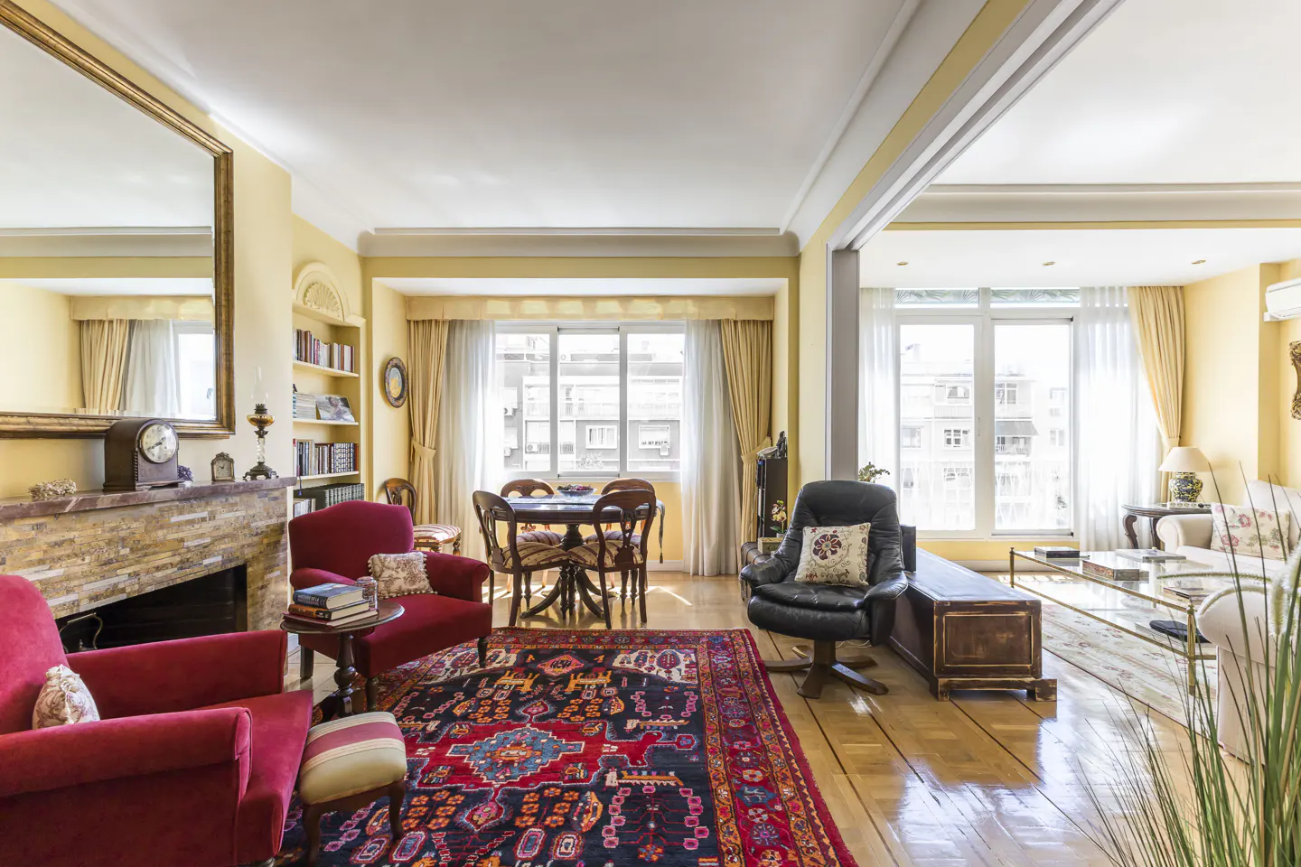 A living room with red armchairs, a fireplace, a dining table, and a black leather chair.